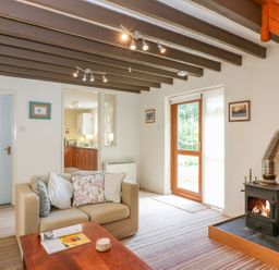 A living room with a beige sofa pillows coffee table a wood burning stove and a door to the outside at Woodstock Cottage Birchill near Chardstock