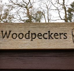 A wooden sign with the word Woodpeckers and a woodpecker illustration at Woodpeckers in Willand