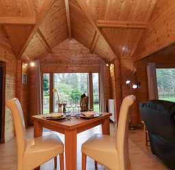 A wooden dining room with a table set for two and cream chairs at Woodpeckers in Willand