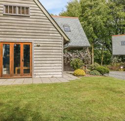 An exterior view of wooden cladded buildings with patios a garden and trees at Trevinny Lodge No 37 in Davidstow near Boscastle
