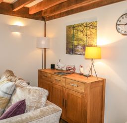 A living room corner with a beige sofa and wooden cabinet with lamps and decorative items at Trevinny Lodge No 37 Davidstow near Boscastle