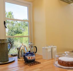 A kitchen with a cake on a stand and tea set at Pheasant Cottage in Priston Village, BATH