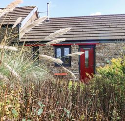 A cottage with a red door and windows surrounded by plants at Farmhand Cottage near Narberth