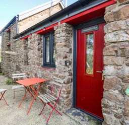 An outdoor area with a red door and stone wall at Farmhand Cottage near Narberth