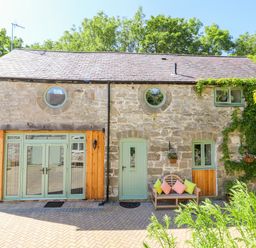 A stone house with green doors and windows with a bench and colorful cushions outside at The Old Coach House in Llanarmon-Yn-Ial