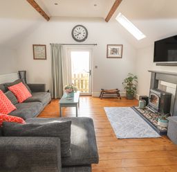 A living room with grey sofas and red cushions a coffee table and a fireplace with a television above at The Old Coach House in Llanarmon-Yn-Ial