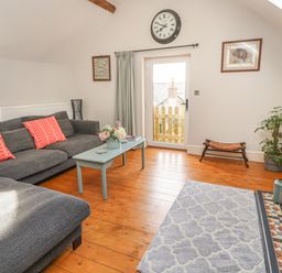 A sitting room with a gray sofa red cushions a coffee table a wall clock and a fireplace at The Old Coach House in Llanarmon-Yn-Ial