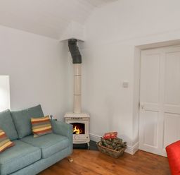 A room with a blue sofa, a burning stove, a basket of firewood, and a red chair at The Old White Cottage in Shillelagh County Wicklow