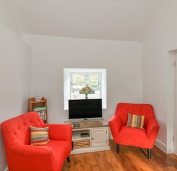 A small sitting room with two red armchairs a television on a cabinet and a small bookshelf at The Old White Cottage in Shillelagh County Wicklow