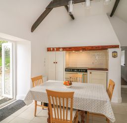 A dining area with a table covered with a patterned tablecloth and four wooden chairs next to a kitchen space with a stove and cupboard at The Old White Cottage in Shillelagh County Wicklow