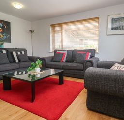 A living room with three grey sofas a black coffee table on a red rug and artwork on the walls at Tremar Carbis Bay
