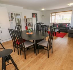 A dining area with a black table and six chairs next to a living room with gray sofas and a red rug at Tremar in Carbis Bay