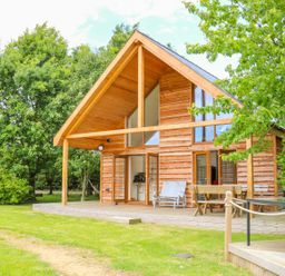 A wooden cabin with a covered porch and outdoor seating surrounded by trees at Dorado Lodge in Thorpe-on-the-Hill