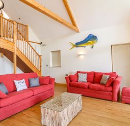 A living room with red sofas wooden staircase and a fish decoration on the wall at Dorado Lodge in Thorpe-on-the-Hill