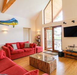 A living room with red sofas a mounted fish a wooden coffee table a wall mounted TV and glass doors at Dorado Lodge in Thorpe-on-the-Hill
