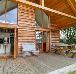 A wooden deck with metal and wooden outdoor furniture outside a log cabin with large windows at Dorado Lodge in Thorpe-on-the-Hill