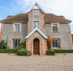 A two-story house with arched windows and a wooden door surrounded by gravel and bushes at Southrepps Lodge in Southrepps