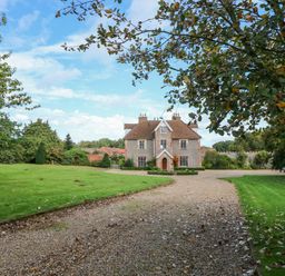 A large stone house at the end of a gravel driveway with lawn and trees around at Southrepps Lodge in Southrepps