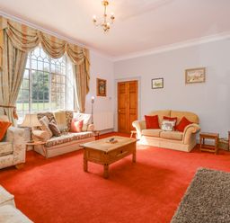 A living room with sofas a wooden coffee table a large window with curtains and a television at Southrepps Lodge in Southrepps