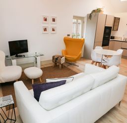A living room with white and yellow chairs a glass TV stand and a round dining table at Sunshine Cottage in Preston under Scar near Leyburn