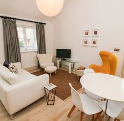 A living room with white sofa round dining table orange armchair and television at Sunshine Cottage Preston under Scar near Leyburn