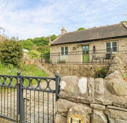 Stone cottage with green door and windows behind black metal gate and stone wall at Sunshine Cottage in Preston under Scar near Leyburn
