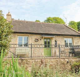 A stone cottage with a green door two windows and metal railing in front at Sunshine Cottage in Preston under Scar near Leyburn
