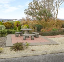 A stone table with four stone benches on a tiled area surrounded by plants and bushes at Ellens Cottage in Mount Charles County Donegal