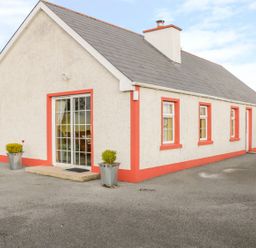 An exterior view of a single-story house with a grey roof and white walls with red trim around windows and doors at Ellens Cottage Mount Charles County Donegal