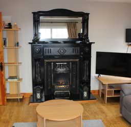 A living room with a black fireplace a wooden door a wooden shelf a TV on a stand a gray couch and a round wooden coffee table at Ellens Cottage in Mount Charles County Donegal