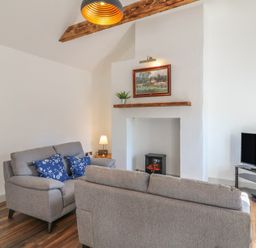 A living room with two gray sofas a small fireplace and a TV on a stand at Macreddin Rock Holiday Cottage Macreddin Aughrim County Wicklow