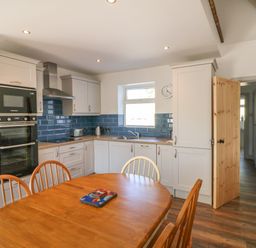 A kitchen with white cabinets blue backsplash wooden dining table and chairs at Macreddin Rock Holiday Cottage Macreddin Aughrim County Wicklow