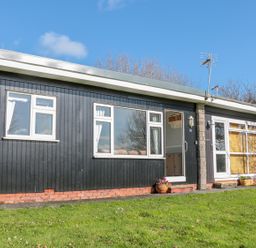 A single story building with black wooden siding windows and a door on a grassy area at The Borrowers in Dartmouth