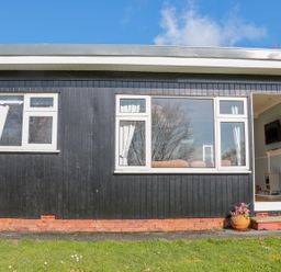 The exterior of a black wooden building with white framed windows and an open door showing a television and stove inside at The Borrowers in Dartmouth