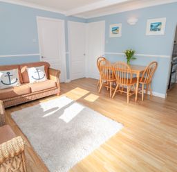 A living room with wicker sofa and armchair pillows with anchors wooden dining table and chairs with flowers on table at The Borrowers in Dartmouth