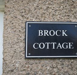 A black and white sign reading Brock Cottage mounted on a pebble textured exterior wall