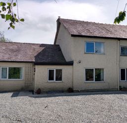 A two-story building with multiple windows and a gravel area in front at Plas Marchog Annexe in Rhoscefnhir near Pentraeth