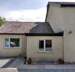 The exterior of a cream-colored building with a gravel and stone pathway and potted plants at Plas Marchog Annexe in Rhoscefnhir near Pentraeth