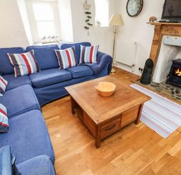 A living room with a blue sofa with striped cushions a wooden coffee table and a fireplace with a fire burning at Labour in Vain in St Ives