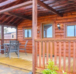 A wooden porch with a round table and four metal chairs at Alken Cabin in Bushmills County Antrim