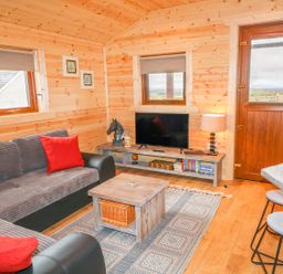 A living room with a sofa a wooden coffee table a TV on a stand and stools at Alken Cabin in Bushmills County Antrim