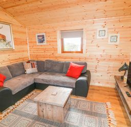 A living room with a sectional sofa a wooden coffee table a rug and a television at Alken Cabin in Bushmills County Antrim