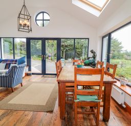 A dining area with a wooden table and chairs next to large windows and a sitting area with a sofa and armchair at The Mermaid in Dungloe County Donegal