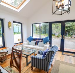 A sitting area with a white sofa and striped armchair around a glass coffee table near large windows and a skylight at The Mermaid in Dungloe County Donegal