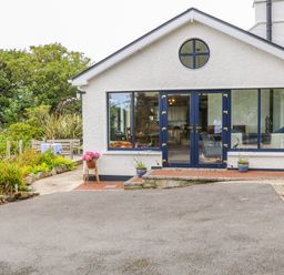 Exterior view of a white house with blue doors and windows surrounded by plants and a paved driveway at The Mermaid in Dungloe County Donegal