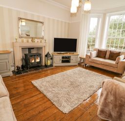 A living room with beige sofas a television on a cabinet a fireplace and large windows at Penholm in Penmaenmawr