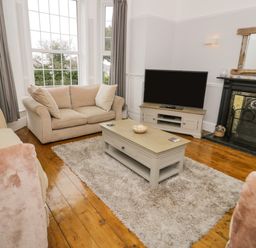 A living room with two beige sofas a wooden coffee table and a TV on a stand at Penholm in Penmaenmawr