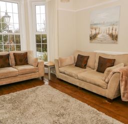 A living room with two beige sofas a wooden floor a beige rug and a painting on the wall at Penholm in Penmaenmawr