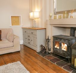 A living room with a beige sofa a gray cabinet with a lamp a black wood stove fire a mirror and a large lantern at Penholm in Penmaenmawr