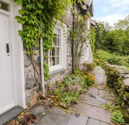 A stone pathway with plants and flowers beside a stone house with white door and windows at Llety Perygl in Harlech